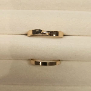Två stilrena guldringar - Säljer två enkla och eleganta guldringar. Den ena ringen har en twistad design medan den andra är klassiskt slät. Perfekta för dig som gillar minimalistiska smycken med en modern touch.