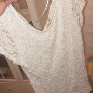 Vit spetsklänning med dragkedja - Superfin vit T-shirt från Cubus med spetsdetaljer över hela tröjan och korta ärmar. Tröjan har en snygg dragkedja i ryggen och är perfekt för sommarens alla tillfällen. Den har en feminin och romantisk look med blommig spets och rund halsringning.