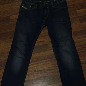 Mörkblå Diesel jeans straight fit - Snygga mörkblå jeans från Diesel med klassisk femficksdesign och diskreta slitningar. Modellen har raka ben och normal passform. Materialmixen består av bomull, viskos, polyester och elastan för skön stretch och komfort. Perfekt för dig som gillar stilrena jeans med lite edge.