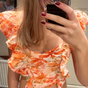 Blommig croppad blus från H&M - Superfin croppad blus från H&M i linneblandning med blommigt mönster i orange, beige och grönt. Toppen har puffiga korta ärmar, omlottdetaljer och snygg rynkning framtill. Perfekt för sommarens alla tillfällen!