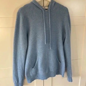 Ljusblå hoodie i kashmir - Mjuk och lyxig ljusblå hoodie från Soft Goat i kashmir. Tröjan har huva med snörning, magficka och ribbade muddar vid ärmslut och nederkant. Perfekt för dig som gillar stilren och bekväm look. Snygg att matcha med jeans eller joggers.
