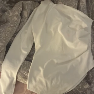 Vit långärmad topp från Bikbok - Säljer en stilren vit polotopp från Bikbok i storlek M. Toppen har en lång ärm och hög krage, tillverkad i ett mjukt och lätt material som ger en clean look. Perfekt för att skapa en snygg layering eller bäras som den är. Fräsch och enkel att matcha med allt.