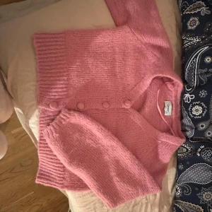Rosa stickad kofta från ONLY - Supermysig rosa stickad kofta från ONLY i storlek S. Koftan har långa ärmar, ribbade muddar och knappar framtill i samma färg som plagget. Perfekt för att addera lite färg till din outfit och hålla dig varm under kyliga dagar.
