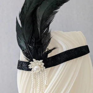 Svart Gatsby-hårdekoration med fjädrar och pärlor - Svart hår dekoration med pärlor, fjädrar och glittrande band. Dekorerat med pärlor och fjädrar för extra glam. Perfekt accessoar för att sticka ut och ge din look en lyxig vintagekänsla. Aldrig använd.