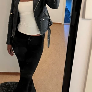 Svarta bootcut kostymbyxor med fickor - Snygga svarta bootcut kostymbyxor med klassisk passform och två bakfickor med knapp. Byxorna har bälteshällor och stängs med knapp och dragkedja framtill. Materialet är mjukt och stretchigt, perfekt för en trendig och bekväm look.