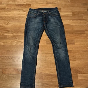 Nudie Jeans Tight Terry Mid Used Saver - Snygga mörkblå jeans från Nudie Jeans, modell Tight Terry Mid Used Saver. Slim fit med klassisk femficksdesign och orangea sömmar. Tillverkade av 99% ekologisk bomull och 1% elastan för skön stretch. Perfekt passform och stilren look.