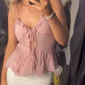 Rosa volangblus med snörning - Säljer en superfin ljusrosa blus med volanger och smala axelband. Toppen har v-ringning, snörning framtill och är tillverkad i ett tunt, luftigt material som ger en flowy känsla. Den är från Zara!