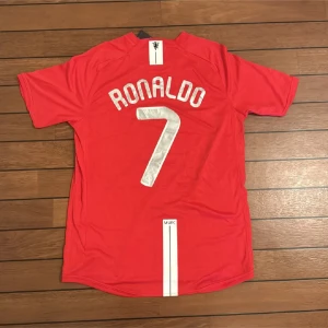 Manchester United Ronaldo 7 Finaltröja - Säljer en officiell Manchester United fotbollströja från Champions League-finalen 2008 med Ronaldo och nummer 7 på ryggen. Tröjan är röd med vita detaljer, AIG-logga på bröstet och broderad text om finalen i gult. Materialet är lätt och andas, perfekt för match eller samling.
