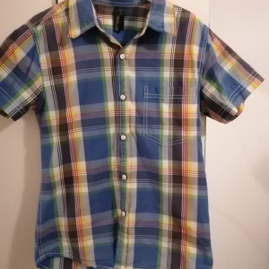 Rutig kortärmad skjorta Next Level - Färgglad rutig skjorta från Next Level med korta ärmar och klassisk krage. Skjortan har tryckknappar framtill, bröstficka och coolt tryck på ryggen med texten 'Official Champions Oldschool'. Materialet är mjuk bomull i blå, grön, gul och röd ton.