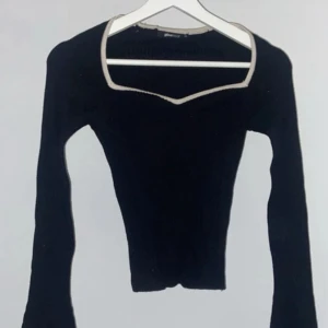 Svart ribbad långärmad topp från Gina Tricot - Svart ribbad långärmad topp från Gina Tricot med ljus kant runt den fyrkantiga halsringningen. Slim fit och croppad längd, ärmarna är långa och sitter tight. Perfekt för dig som gillar minimalistisk stil med en twist.