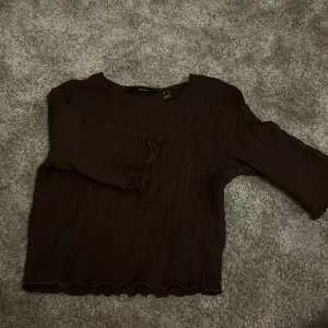 Brun topp från Vero Moda med struktur - Säljer en brun topp från Vero Moda i storlek S. Toppen har en crinklad struktur, trekvartsärm och vågiga kanter vid ärmslut och nederkant. Passformen är normal och materialet känns lätt och skönt mot huden. Perfekt för dig som gillar stilrena och enkla plagg.