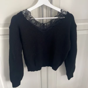 Svart stickad tröja med spetsdetalj - Svart stickad tröja med lång ärm och snygg v-ringning dekorerad med svart spets. Snygg att ha one off shoulder med spets bh. 