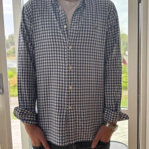 Blårutig skjorta från Ralph Lauren - Snygg blårutig skjorta från Ralph Lauren i slim fit-modell. Skjortan har klassisk button down-krage, vita knappar och broderad logga på bröstet. Tillverkad i mjuk bomull och har långa ärmar. Perfekt för dig som gillar preppy stil.