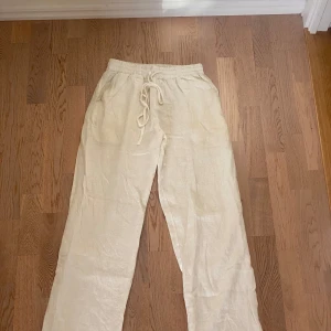 Vita linnebyxor med snörning från Amare - Luftiga vita linnebyxor från Amare i storlek M. Byxorna har elastisk midja med snörning och raka ben. Perfekta för varma dagar när du vill ha en chill och avslappnad look. Lite smutsiga på rumpan men det är knappt synligt därav det billiga priset. Köpte dom för 999kr