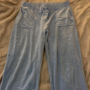 Ljusblå juicy velour byxa - Säljer ett par ljusblå juicy byxor i storlek XL(sitter mer som L). Har varit använda, och visar mindre tecken på användning såsom en tappad silver detalj vid snöret. Köptes för 1 200 kr, men säljer den nu för ett billigt pris. 🩵