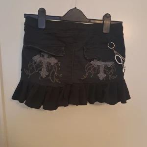 Minikjol med plisserad volang - Kjol med resår i midjan, fickor i sidorna. Broderi på baksidan. Byxhyllsor enligt bild. Barnstorlek men ska passa xs-s, eventuellt M. 🩷 Kan inkludera kedjan om så önskas.    Mått (cm) Midja: 37 Längd: 27