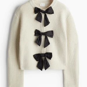 Beige stickad kofta med svarta rosetter - Superfin vit stickad kofta med tre stora svarta rosetter framtill. Det är knappar vid rosetterna så man kan ha den både öppen eller stäng! Sticks inte, nypris 499kr, använd 1 gång