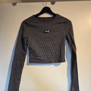 Randig croppad långärmad topp - Säljer en croppad långärmad topp. Toppen är ribbad och har en liten broderad logga framtill. Perfekt för dig som gillar en enkel men snygg stil.