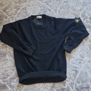 Stone Island Sweater - Svart sweatshirt från Stone Island med klassisk rund hals och ribbade muddar. Ikonisk logotyp-patch på vänster ärm. Tillverkad i mjuk bomull för en clean och stilren look. Perfekt för dig som gillar streetwear och vill ha något enkelt men ändå exklusivt.