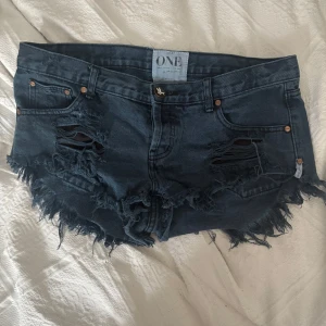 Mörkblå jeansshorts från One Teaspoon - Säljer ett par mörkblå jeansshorts från One Teaspoon, modell Bonitas. De har låg midja, råa kanter och slitna detaljer framtill för en edgy look. Klassisk femficksmodell med knappgylf och fransig avslutning. Ganska stor i storleken!