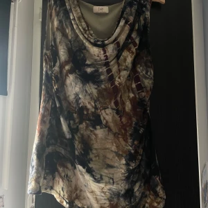 Mönstrad ärmlös topp från Isay - Säljer en cool ärmlös topp från Isay med unikt batikmönster i svart, brun, beige och grå toner. Toppen har en lös passform och snygg draperad halsringning. Perfekt för dig som gillar att sticka ut med din stil.