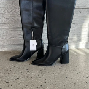 Svarta stövlar från Stradivarius - Snygga svarta stövlar från Stradivarius med spetsig tå och bred klack. Skorna är i skinnimitation och har dragkedja på insidan. Skorna är oanvända. 