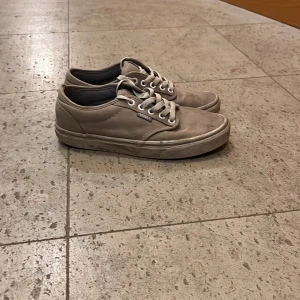 Beige Vans sneakers med snörning - Säljer ett par klassiska beige Vans sneakers med lågt skaft och vit snörning. Skorna har rund tå, platt sula och är tillverkade i canvas med diskret Vans-logga på sidan. Perfekta för en avslappnad streetstil.