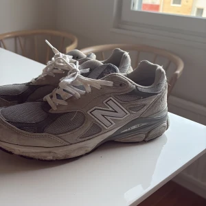 Grå New Balance 990 sneakers - Säljer ett par klassiska New Balance 990 sneakers i grått med vita detaljer. Skorna har meshpaneler och mockadetaljer, samt den ikoniska N-loggan på sidan. Sulan är robust och ger bra stöd. Perfekta för dig som gillar retrovibbar och streetstyle.