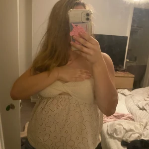 Beige ärmlös blus med broderade blommor - Supersöt beige blus med broderade blommor och twistad bandeau-liknande överdel. Toppen är ärmlös och har en luftig passform med fina hålbroderier i blommönster. Perfekt för varma dagar och ger en romantisk vibe.