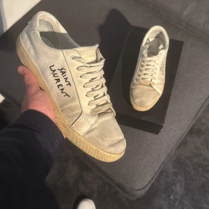 Saint Laurent vita sneakers i canvas - Säljer nu mina gamla snygga sneakers från Saint Laurent de dem inte passar mig så bra längre. Skorna har andvänds ganska mycket och har därför tydliga tecken på andvändning. Inga defekter dock. Strl 43 men kan funka på ngn som har 42 
