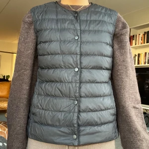 Svart dunväst från Uniqlo - Säljer en svart, quiltad dunväst från Uniqlo. Västen är lätt och har tryckknappar framtill samt rund halsringning. Perfekt att slänga över en hoodie eller tröja när det är kyligt ute. Klassisk och stilren design som funkar till det mesta.