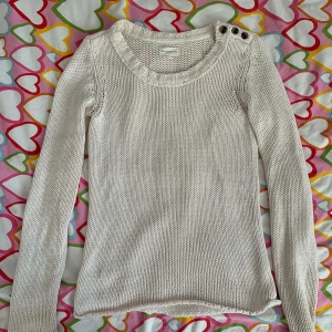 Vit stickad tröja med knappar - Vit stickad tröja från 365 Sunshine med rund halsringning och tre snygga knappar på axeln. Långärmad och i mjukt material som passar perfekt till lager-på-lager. Enkel och stilren design som funkar till det mesta.