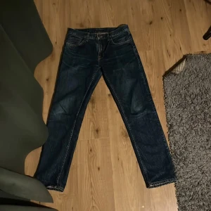 Nudie Jeans Gritty Jackson Dark Space 30/32 - Säljer ett par mörkblå Nudie Jeans Gritty Jackson i modellen Dark Space. Klassisk femficksdesign, raka ben och snygga kontrastsömmar. Tillverkade i 100% bomull för en autentisk jeanskänsla. Perfekta för dig som gillar stilrena och tidlösa jeans.