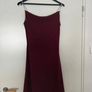 Vinröd klänning med strassband Vero Moda - Vinröd kortklänning från Vero Moda med smala axelband dekorerade med strass. Klänningen har en enkel, rak passform och är ärmlös. Materialet är mjukt och följsamt, perfekt för dig som vill sticka ut med en elegant touch. Har ett litet märke där nere i klänningen men inget som syns otroligt mycket. 