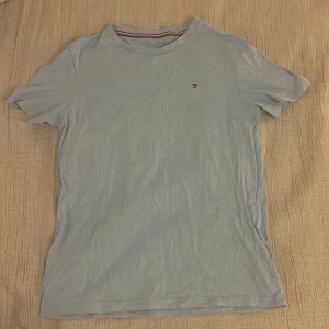 Ljusblå t-shirt från Tommy Hilfiger - Tja! Säljer denna snygga ljusblå t-shirten från Tommy Hilfiger med klassisk logga broderad på bröstet. T-shirten har rund halsringning och korta ärmar. Tillverkad i mjuk bomull för en skön känsla hela dagen. Säljer eftersom den har blivit för liten för mig. Pris kan diskuteras vid snabb affär