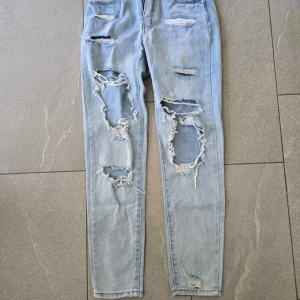 Ljusa ripped jeans med skinny fit - Säljer ett par ljusblå jeans med rejält slitna och trasiga detaljer framtill. Byxorna har skinny passform och är tillverkade i klassiskt jeanstyg. Perfekta för dig som gillar en edgy och trendig stil.