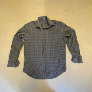 Grå  rutig skjorta med knappar - Snygg grå skjorta med vitt rutmönster och klassisk krage. Skjortan har långa ärmar och knäppning framtill. Perfekt för dig som gillar en stilren och enkel look. Materialet känns mjukt och bekvämt mot huden.