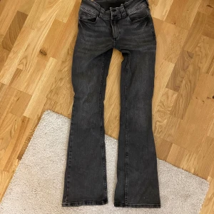 Svarta bootcut jeans med fickdetaljer - Snygga svarta jeans med bootcut passform och coola fickdetaljer bak med knappar. Jeansen har klassisk femficksdesign och är tillverkade i stretchigt denimtyg som sitter skönt. Perfekta för dig som gillar en lite utsvängd look.