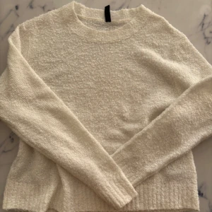 Vit stickad tröja med rund hals - Mysig vit stickad tröja med rund halsringning och långa ärmar. Tröjan har en lite fluffig struktur och ribbade muddar vid ärmslut och nederkant. Perfekt för lager-på-lager och chill dagar.
