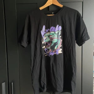 Svart t-shirt med pantermotiv - Cool svart t-shirt med färgstarkt tryck av en panter och texten 'Brave Spirit' i lila och turkos. T-shirten har rund hals och korta ärmar, perfekt för en streetwear-look.