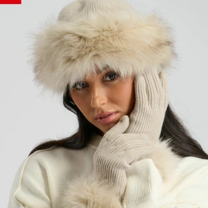 Beige stickad mössa med päls - Snygg beige stickad mössa med bred, fluffig pälsdetalj runt kanten. Mössan har en klassisk form och är perfekt för kalla dagar när du vill hålla stilen. Passar dig som gillar en lyxig och trendig vinterlook.