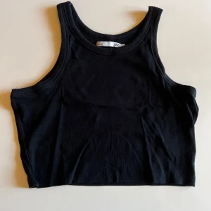 Svart ribbad linnetopp från 157 - Säljer en svart ribbad linnetopp från 157. Toppen är croppad med breda axelband och rund halsringning. Perfekt för lager-på-lager eller till ett par höga jeans. Enkel och stilren design som funkar till många olika looks.