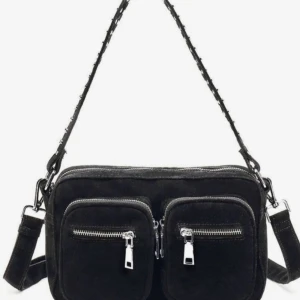 Svart mocka axelväska med dragkedjor - Snygg svart axelväska i mocka med två framfickor och silvriga dragkedjor. Väskan har justerbar axelrem och flera fack för smart förvaring. Perfekt för dig som vill ha en stilren och praktisk väska till vardagen.