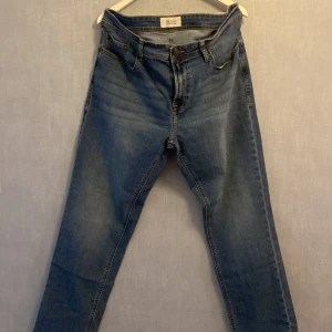 Blå jeans från Stock & Hank W40 L32 - Klassiska blå jeans från Stock & Hank, modell SH EASE. Jeansen har fem fickor, gylf med dragkedja och knapp, samt kontrastsömmar. Tillverkade i slitstarkt denimtyg som ger en tidlös look. Perfekta för dig som gillar en enkel och clean stil.