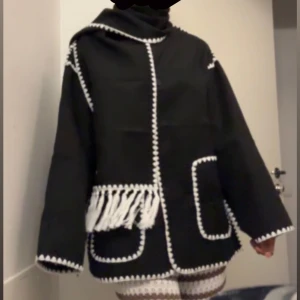 Svart kappa - Svart kort kappa med vita virkade kanter med fransk halsduk, oversized passform. Perfekt för dig som gillar unika detaljer och kontraster.