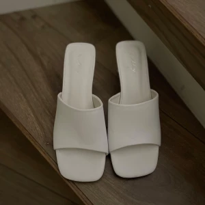 Vita klack skor dinsko  - Säljer ett par stilrena vita  med låg klack och fyrkantig tå. Skorna har öppen häl och bred rem över foten, vilket ger en modern och minimalistisk look. Perfekta för dig som gillar enkel men trendig design.