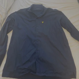 Mörkblå skjorta från Lyle & Scott - Snygg mörkblå skjorta från Lyle & Scott med klassisk krage och knappar framtill. Bröstficka med gul broderad logga. Perfekt för dig som gillar stilrena plagg. Använd bara ca 3 gånger