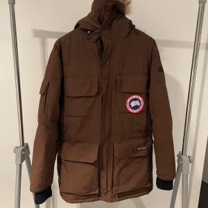 Brun Canada Goose dunjacka med huva - Säljer en brun Canada Goose dunjacka med stor huva och pälskant. Jackan har flera stora fickor framtill, klassisk logga på bröstet och är perfekt för kalla vinterdagar. Materialet är slitstarkt och jackan har en loose passform för extra komfort.     Är för närvarande i Tyskland men frakt möjlig✌️