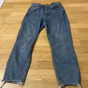 Blå jeans från Vero Moda med råa kanter - Snygga blå jeans från Vero Moda med hög midja och raka ben. Jeansen har klassisk femficksdesign och råa, fransiga benslut för en trendig look. Tillverkade i denim med en skön passform som passar till allt.
