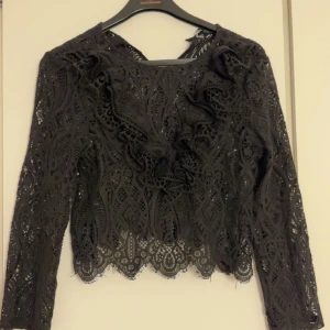 Svart spetsblus med volangdetaljer - Säljer en svart blus i spets med långa ärmar. Aldrig använd!